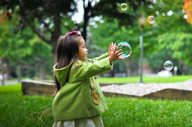 Eszter Fabian - Flicka i gröna kläder leker med såpbubblor.