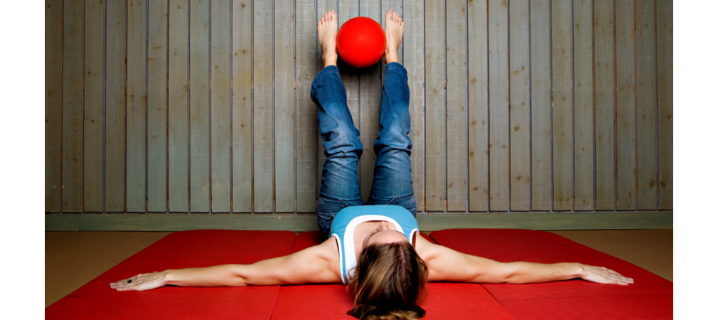 kvinna som ligger på rygg med röd boll mellan fötterna