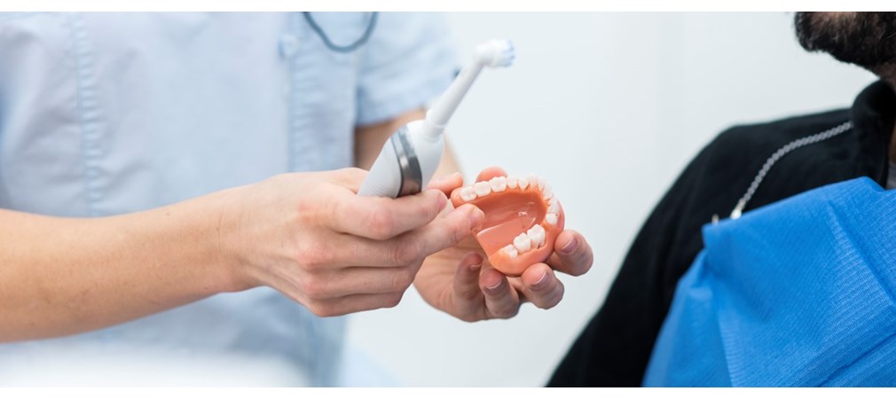 Tandläkare visar upp eltandborste och tandmodell för patient